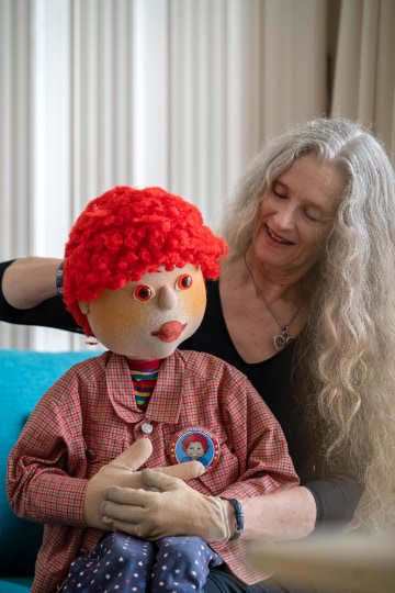 A woman sitting and holding the puppet, Toby.  Toby is used to help deliver prevention programmes in schools.